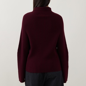 Model wearing Annette Gortz merlot merino wool ribbed knit jumper with turtleneck and wide sleeves, back view.