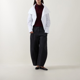 Model wearing Annette Gortz Merlot merino wool knit, styled with white jacket and black wide-leg trousers, black flat shoes.