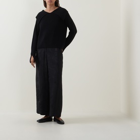 Model wearing Annette Gortz black merino wool V-neck knit, styled with wide-leg dark trousers and flat black loafers.