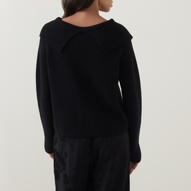Model wearing Annette Gortz black merino wool knit, rear view showing oversized collar detail, styled with black wide-leg trousers.