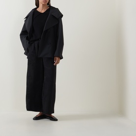Model wearing Annette Gortz black merino wool knitwear, styled with an oversized black coat and wide-leg trousers.