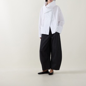 Model wearing Annette Gortz white cotton asymmetric wrap shirt, styled with wide-leg black trousers and black flat shoes.