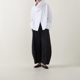 Model wearing Annette Gortz white cotton asymmetric shirt with black wide-leg trousers and black ballet flats.
