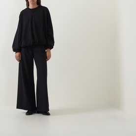 Model wearing Annette Gortz black silk top with balloon sleeves, styled with matching wide-leg black trousers and black flats.