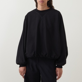 Model wearing Annette Gortz black silk top with elasticated hem, blouson sleeves and crew neck, styled with matching black trousers