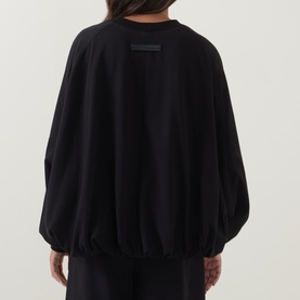 Model wearing Annette Gortz black silk top, rear view, with relaxed balloon sleeves, elasticated hem, and tonal label detail.