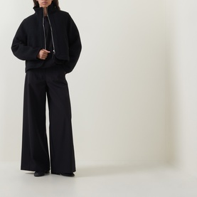 Model wearing Annette Gortz black silk top with half-zip funnel neck, styled with wide-leg black trousers and black shoes.