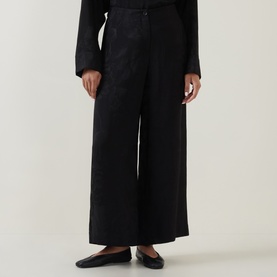 Model wearing Annette Gortz black wide-leg cotton trousers with pleat detail, styled with black blazer and flat loafers.