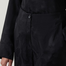 Model wearing Annette Gortz black cotton trousers with subtle jacquard floral pattern, close-up of waistband and button detail.