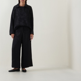Model wearing Annette Gortz black wide-leg cotton trousers, styled with a matching black textured sweatshirt and flat ballet pumps.
