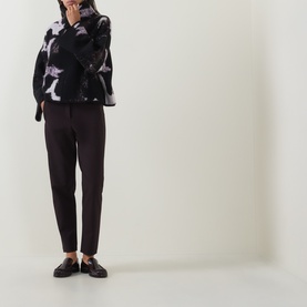 Model wearing Annette Gortz cocoa cotton trousers with a black floral print blouse and black loafers.