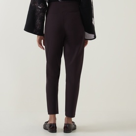 Model wearing Annette Gortz cocoa cotton trousers, rear view, styled with black floral kimono-style top and black loafers.