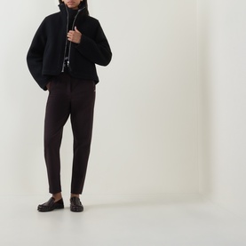 Model wearing Annette Gortz cocoa cotton trousers with a black fleece sweatshirt and dark leather loafers.