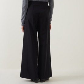 Model wearing Annette Gortz black wide-leg trousers, rear view, styled with a grey long-sleeve top
