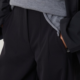 Model wearing Annette Gortz black cotton trousers, close-up of side pocket detail, styled with grey top and black jacket.