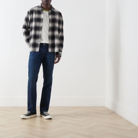 Model wearing Citizens of Humanity dark indigo straight jeans, styled with grey check overshirt, white tee and black canvas trainers.
