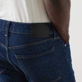 Model wearing Citizens of Humanity Dark Indigo straight jeans, close-up of back pocket with branded label, styled with white tee.