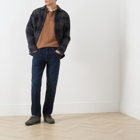 Model wearing Citizens of Humanity Indio straight jeans in dark indigo, styled with a check overshirt, camel knit and grey shoes.