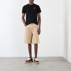 Model wearing Comme Des Gar&ccedil;ons Play black cotton T-shirt with red heart logo, styled with beige cargo shorts and black flatform trainers.