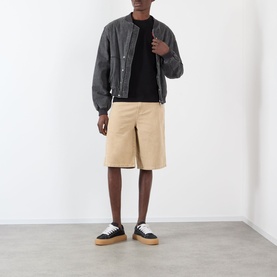Model wearing Comme Des Gar&ccedil;ons Play black cotton T-shirt, styled with grey bomber jacket, beige shorts, and black flatform trainers.