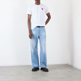 Model wearing Comme Des Garcons Play Double Heart Embroidered Logo T-Shirt in white, styled with light blue wide-leg jeans and black loafers.