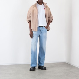 Model wearing Comme Des Gar&ccedil;ons Play Double Heart Embroidered Logo T-Shirt in white, styled with beige zip jacket, light wash jeans and black loafers.