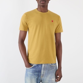Model wearing Comme des Gar&ccedil;ons Play olive cotton T-shirt with small red heart logo patch, styled with light wash jeans.