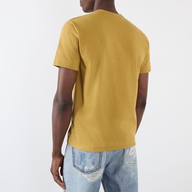 Model wearing Comme des Gar&ccedil;ons Play olive cotton T-shirt, rear view, styled with light wash distressed jeans.