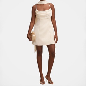Model wearing Forever New Cannoli Cream mini dress with cowl neckline and spaghetti straps, styled with gold heels and clutch bag