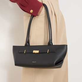 Model carrying DeMellier New York Leather Shoulder Bag in black with gold-tone hardware and signature belt detail, styled with beige wide-leg