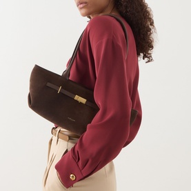 Model carrying DeMellier New York Suede Shoulder Bag in Mocha with gold-tone hardware and signature belt detail, styled with burgundy top and cream