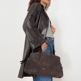 Model carrying DeMellier The Stockholm Midi Top Handle Bag in Dark Chocolate suede with gold hardware, styled with dark leather jacket and jeans