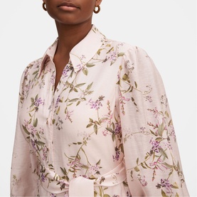 Model wearing pink floral print shirt with botanical purple and green motif, collar neck, relaxed fit, with gold stud earrings visible