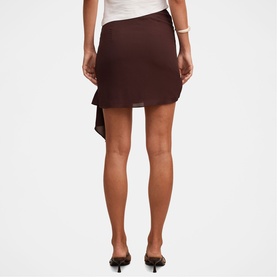 Model wearing a dark brown asymmetric mini skirt with draped panel, styled with a white top and black heeled mules.