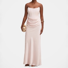 Model wearing blush pink strapless maxi dress with boned corset bodice and ruched skirt, styled with gold clutch bag and bracelet.