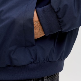 Close-up of navy blue bomber jacket showing ribbed cuff, elasticated hem, and side pocket with model's hand inserted
