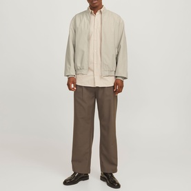Model wearing a light beige bomber jacket, styled with a cream shirt, brown wide-leg trousers, and dark leather shoes