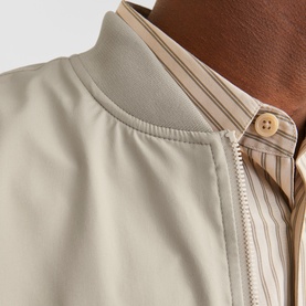 Close-up of a stone beige zip-up bomber jacket collar, styled over a beige striped shirt, showing zip and ribbed neckline detail