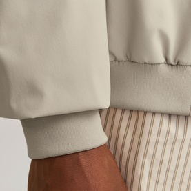 Close-up of a stone beige bomber jacket cuff with ribbed trim, styled over striped trousers