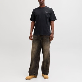 Model wearing black crew neck T-shirt with small chest logo, styled with brown wide-leg jeans and tan boots