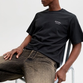 Model wearing Jack & Jones black crew neck T-shirt with script logo, styled with brown wash jeans.
