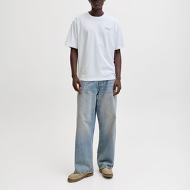 Model wearing white oversized crew-neck T-shirt with light wash wide-leg jeans and beige trainers