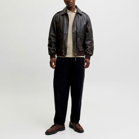Model wearing dark brown leather bomber jacket with ribbed cuffs and hem, styled with beige knit, navy trousers and brown loafers