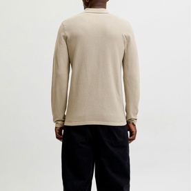 Model wearing a beige long-sleeve polo top, rear view, styled with dark navy trousers