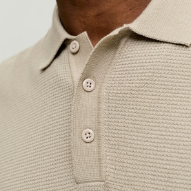Close-up of stone textured knit polo shirt collar and button placket detail, showing tonal buttons and structured weave fabric