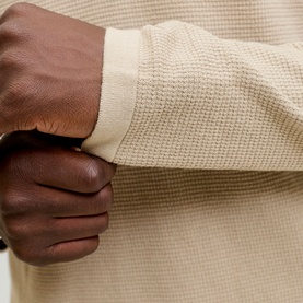 Close-up of cream waffle-knit fabric sleeve cuff, showing textured weave and ribbed hem detail