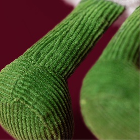 Jellycat Amuseeable plush toy close-up showing green corduroy textured limbs and circular base detail against burgundy background.