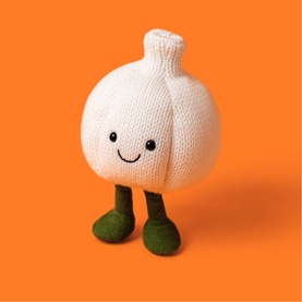 Jellycat Amuseeable white knitted garlic plush toy with smiley face and green legs, shown on orange background