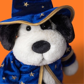 Jellycat plush dog soft toy dressed in navy blue and gold star wizard hat and robe, close-up shot on orange background
