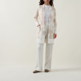 Model wearing Joseph Ribkoff Oatmeal/Winter White floral lace cover-up, styled with white wide-leg trousers and a white top.
